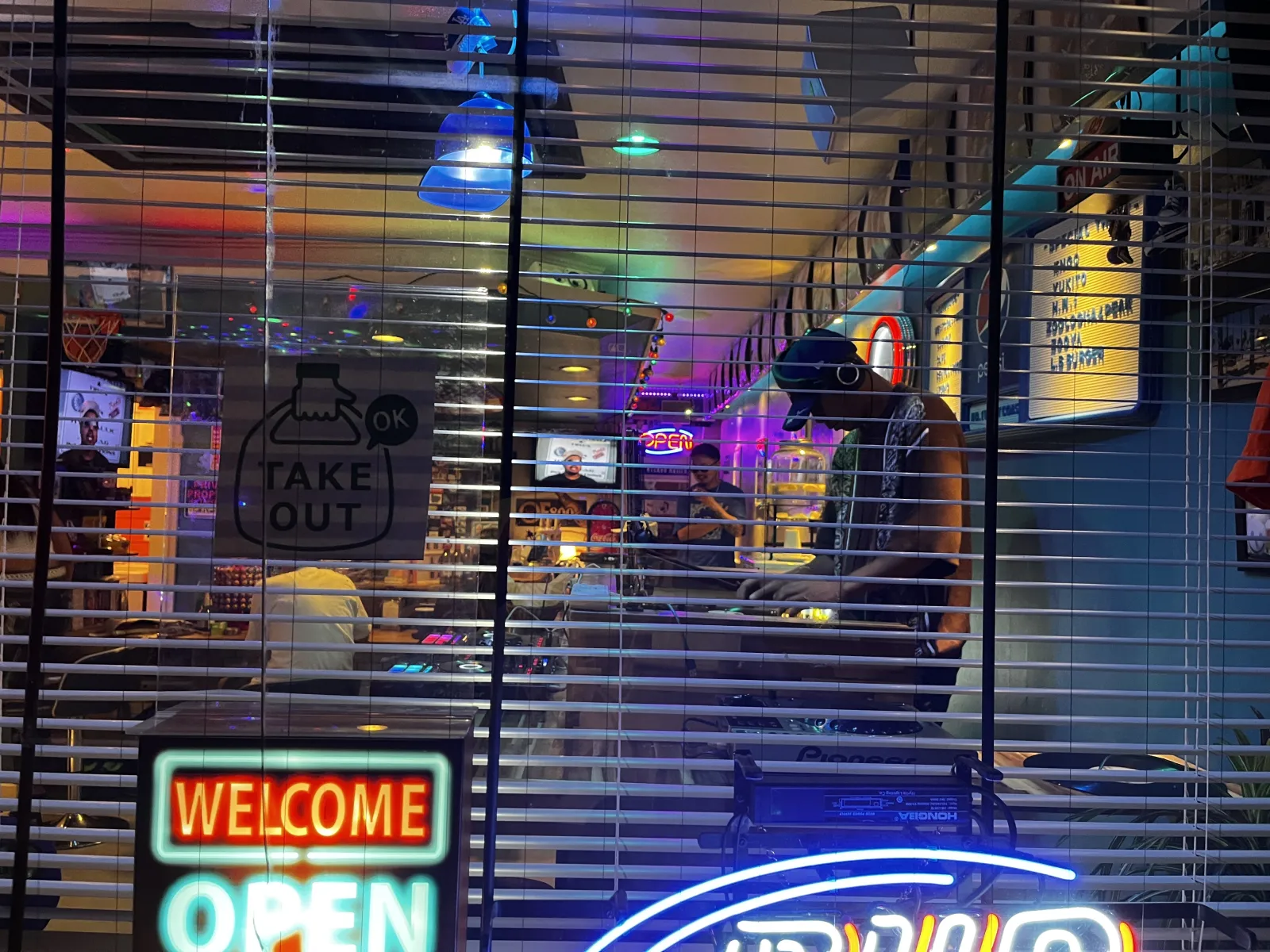 夜、窓越しにDJがデッキを回している様子。紫と青のライトに照らされた店内